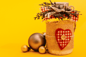 Photo d'un bocal en verre décoré avec des éléments comme du tissu, de la ficelle, des boutons et branches sur fond jaune afin d'emballer ses cadeaux de manière réutilisable
